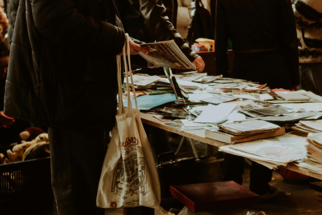 girl holding tote bag while picking up newspaper from table